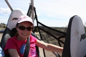 A girl wearing a pink shirt and sunglasses is smiling while seated in a dune buggy.