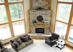 A cozy living room with large windows, a stone fireplace, and comfortable seating.