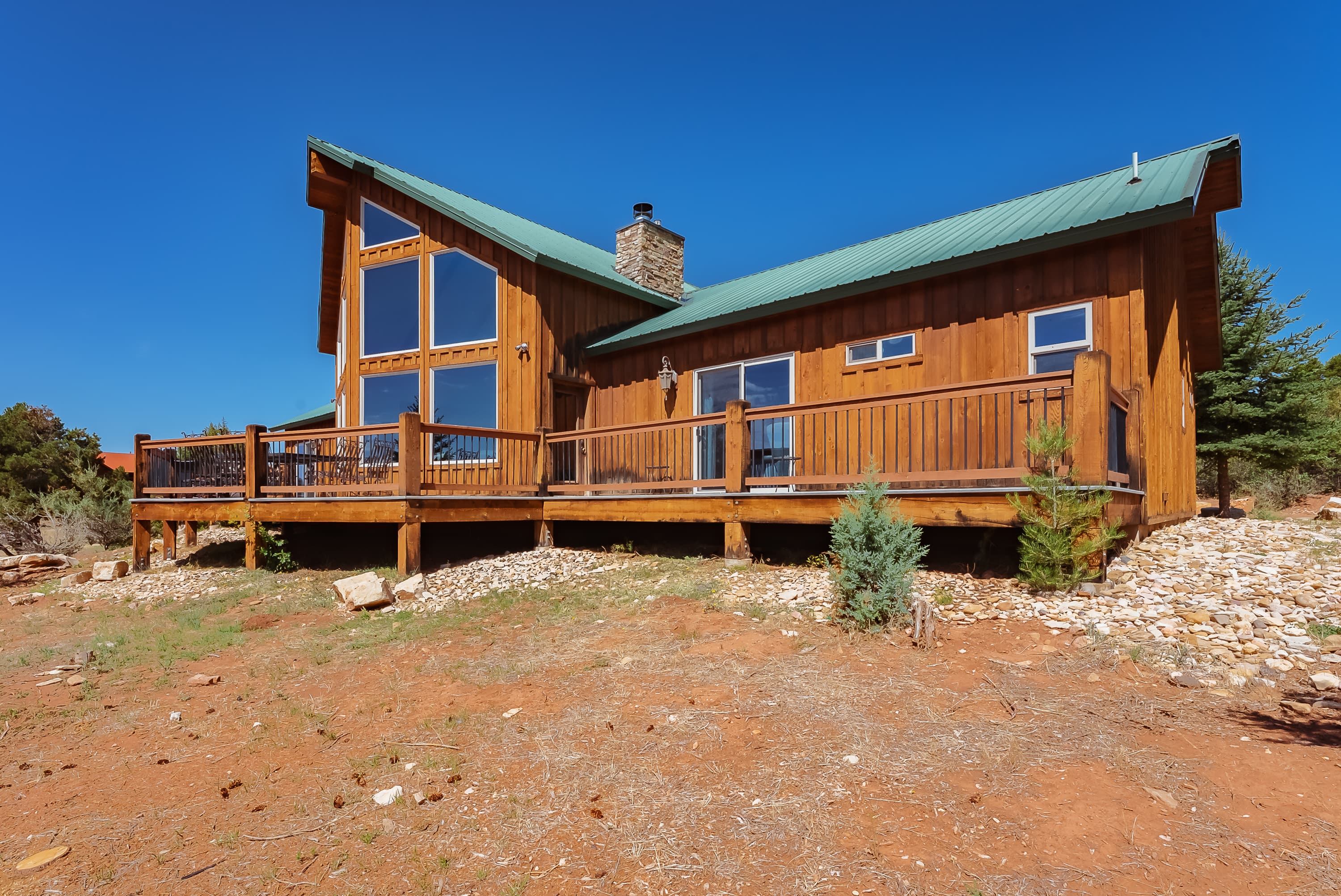A wooden cabin with a green metal roof and large windows, set in a natural landscape.