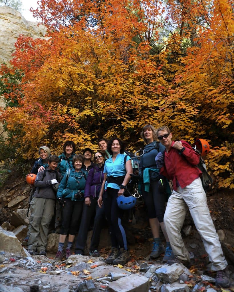 A group of hikers poses in front of vibrant autumn foliage.