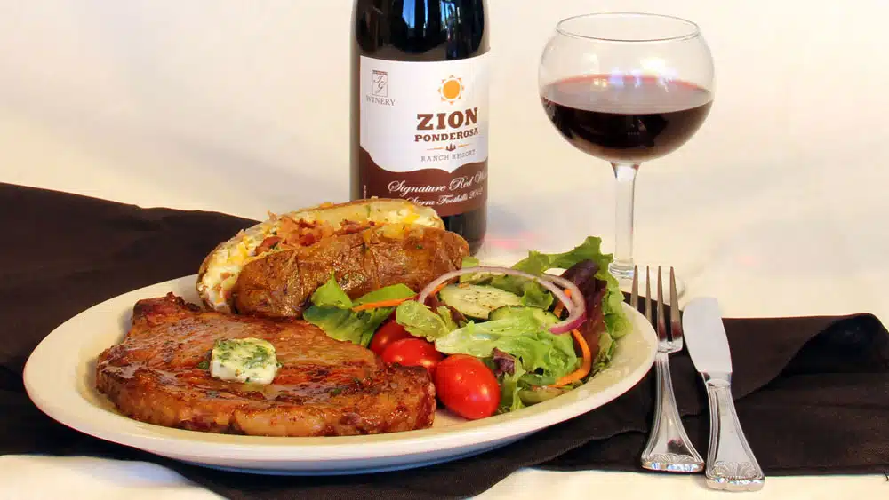 A plate featuring a cooked steak with butter, baked potato, fresh salad, a glass of red wine, and a wine bottle.