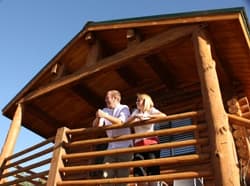 A man and woman stand on the balcony of a wooden cabin, enjoying the view.