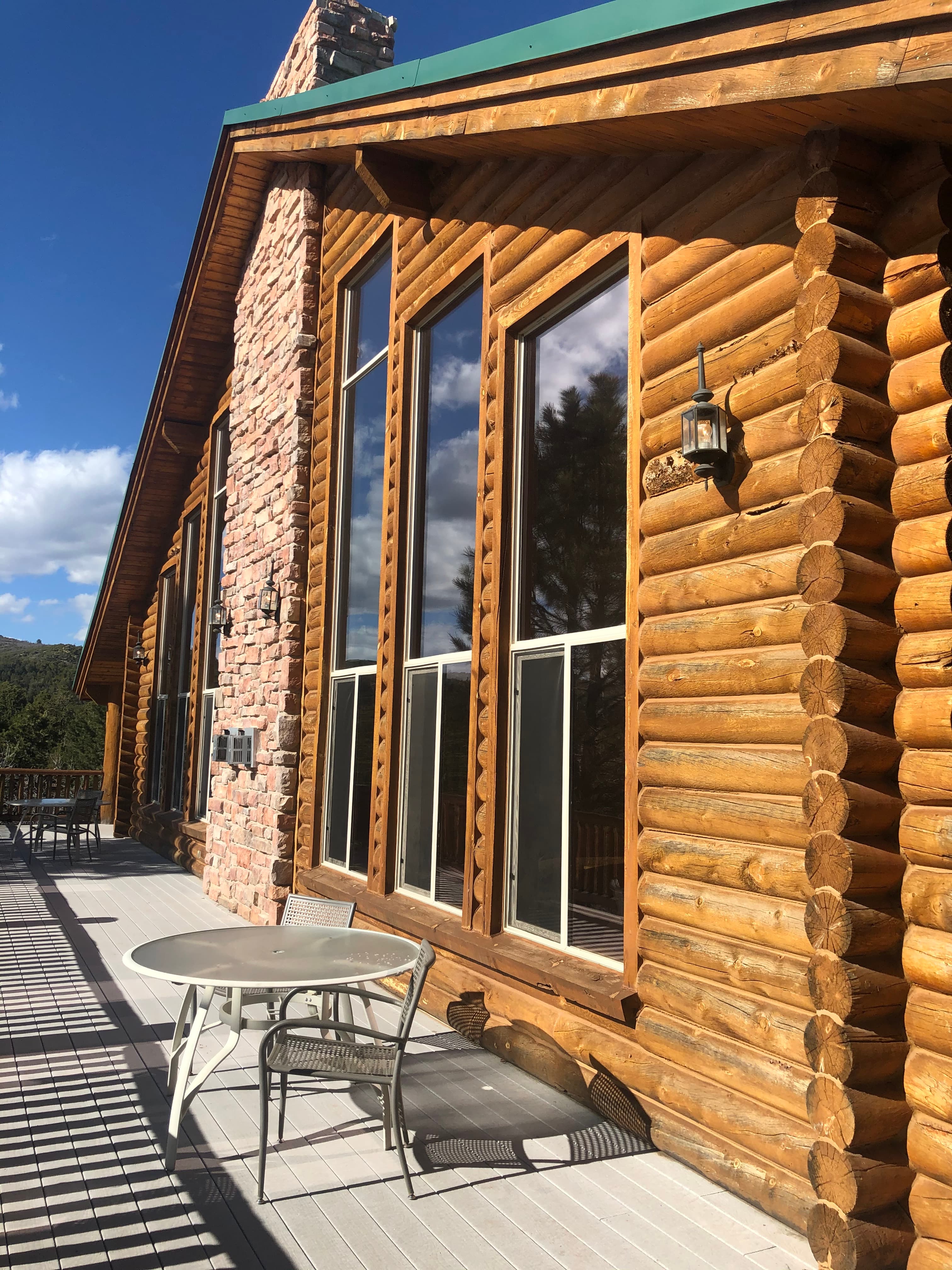 A wooden log cabin with large windows and a small table on the deck under a blue sky.