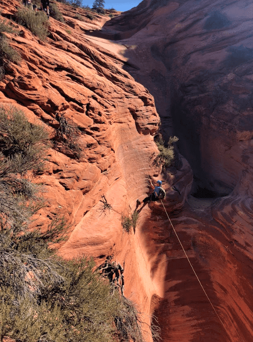 A climber descends a steep, red rock formation using a rope.
