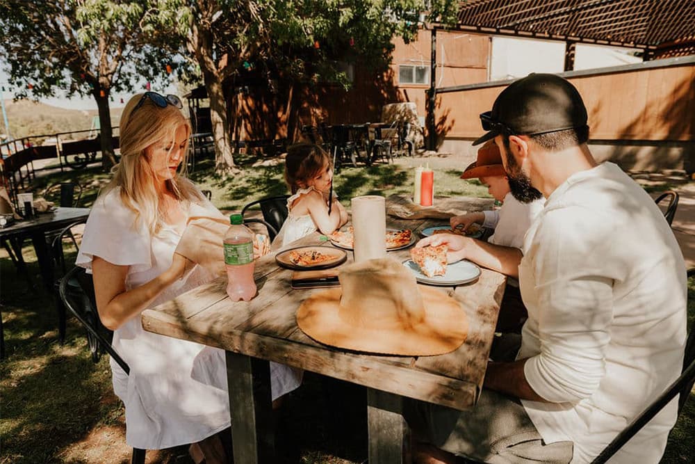 A family enjoys a meal together at an outdoor table under a tree.