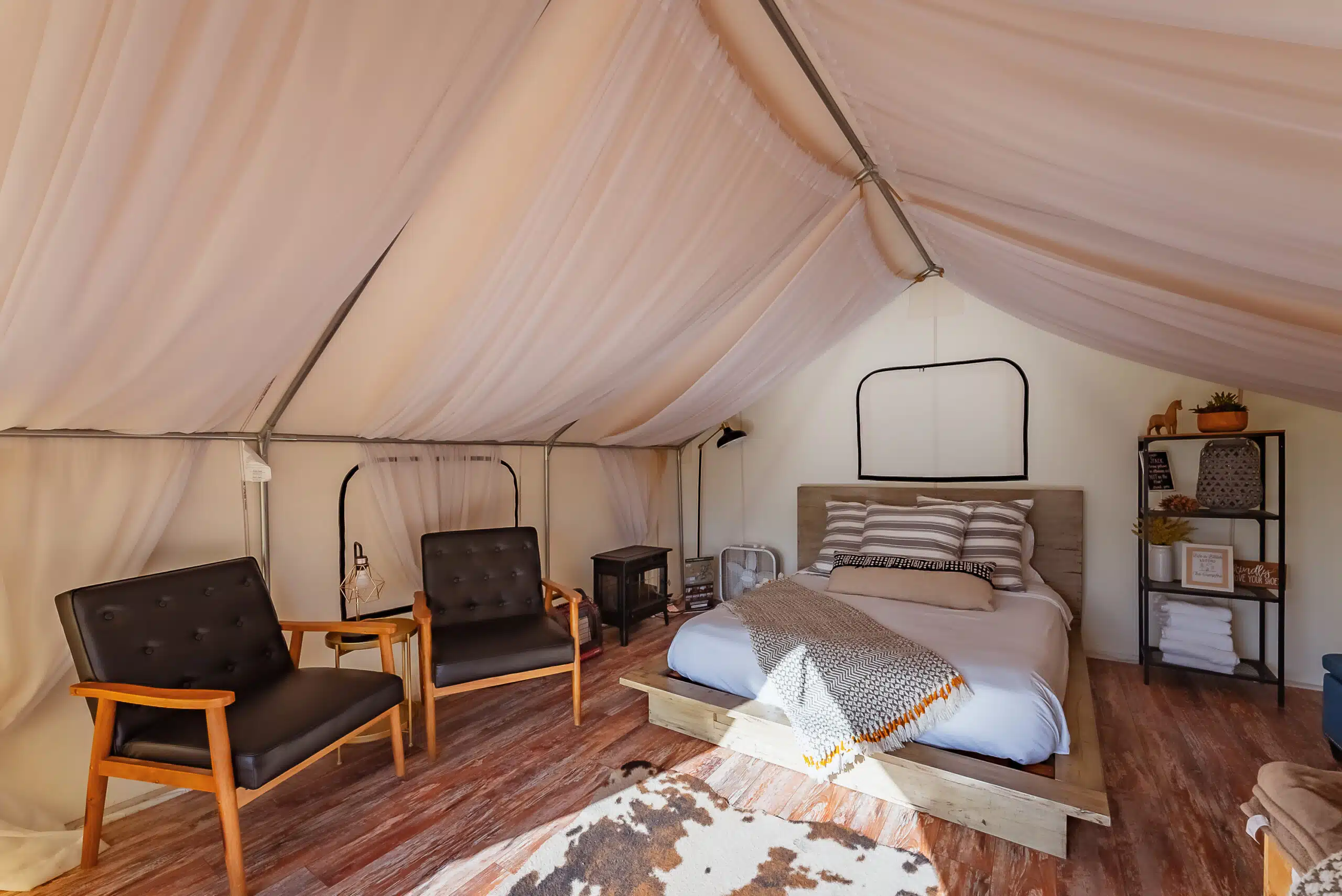 A cozy glamping tent featuring a bed and two chairs.