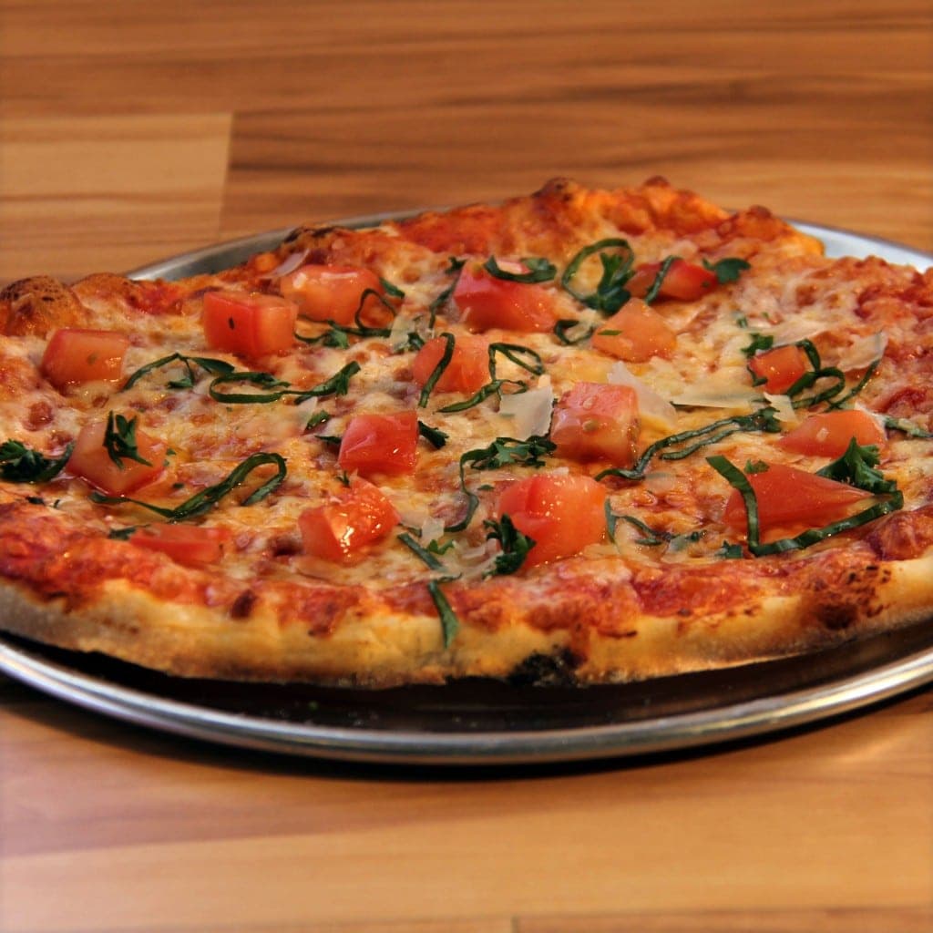 A freshly baked pizza topped with diced tomatoes and basil, on a metal tray.