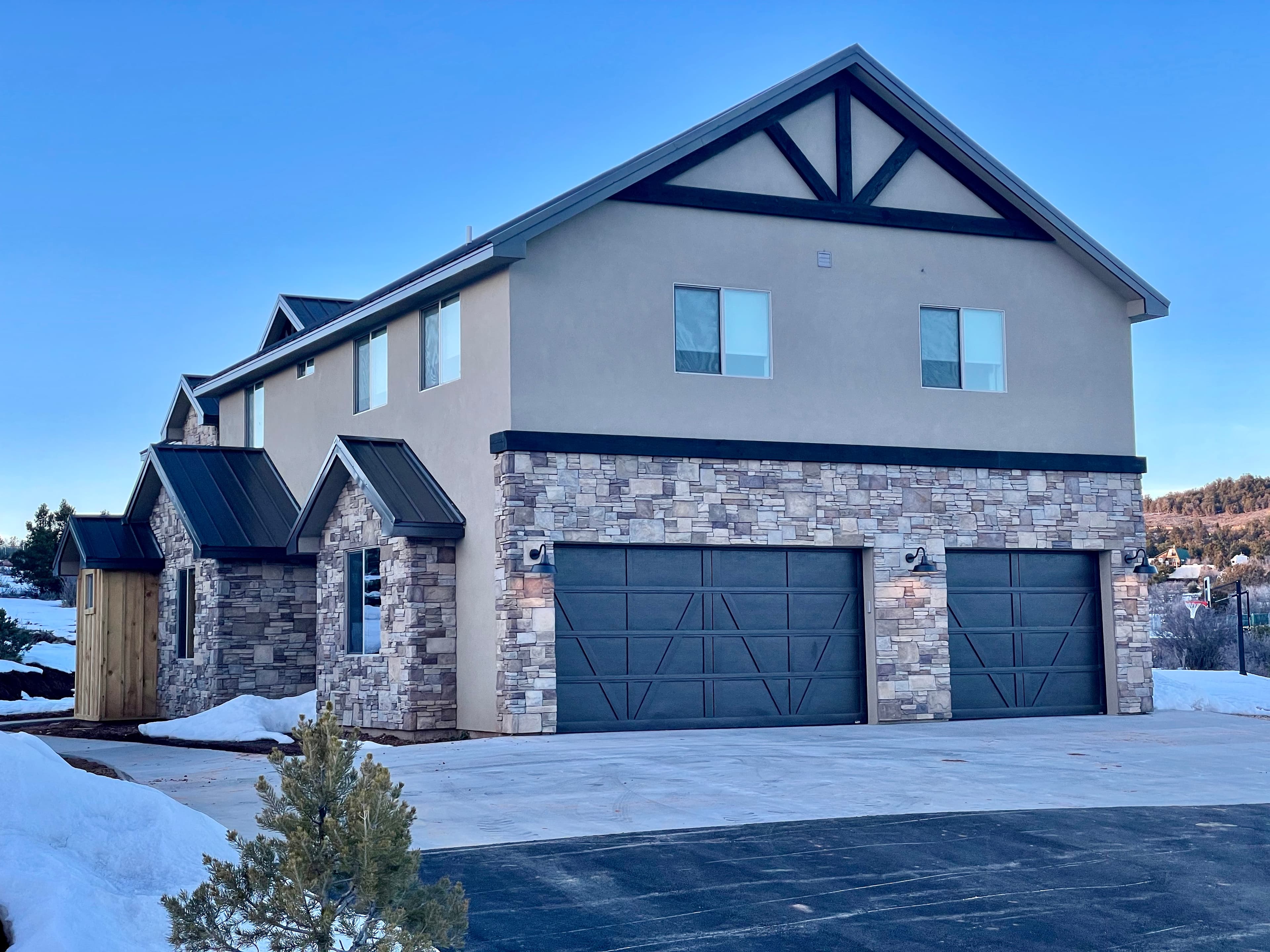 A modern two-story house with a stone facade and two garage doors, surrounded by snow.