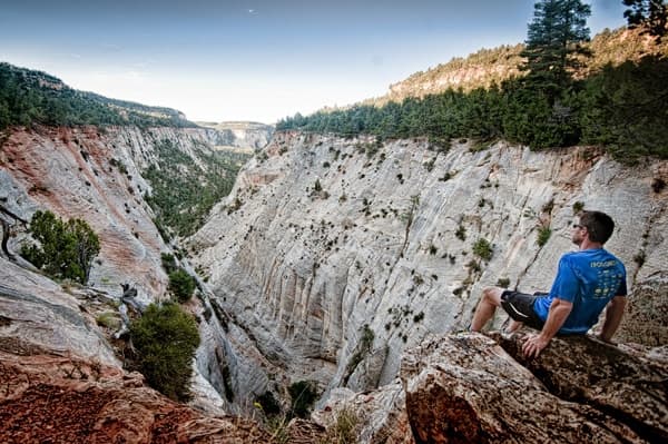 A person rests on a rock while looking out over a deep canyon surrounded by trees.