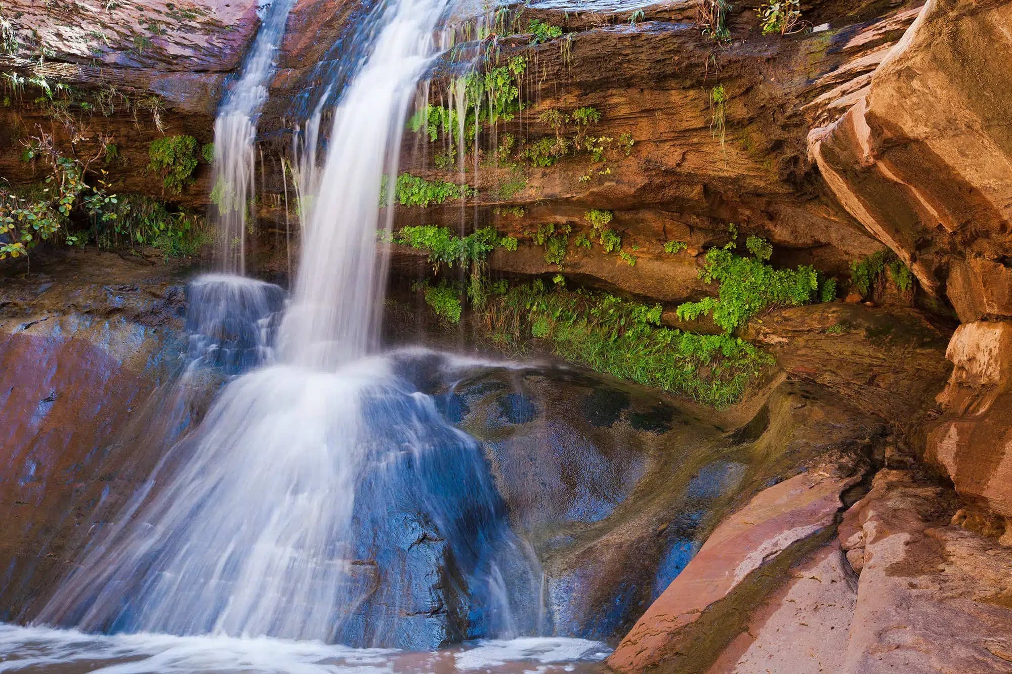 A serene waterfall cascades over rocky cliffs, surrounded by lush greenery.
