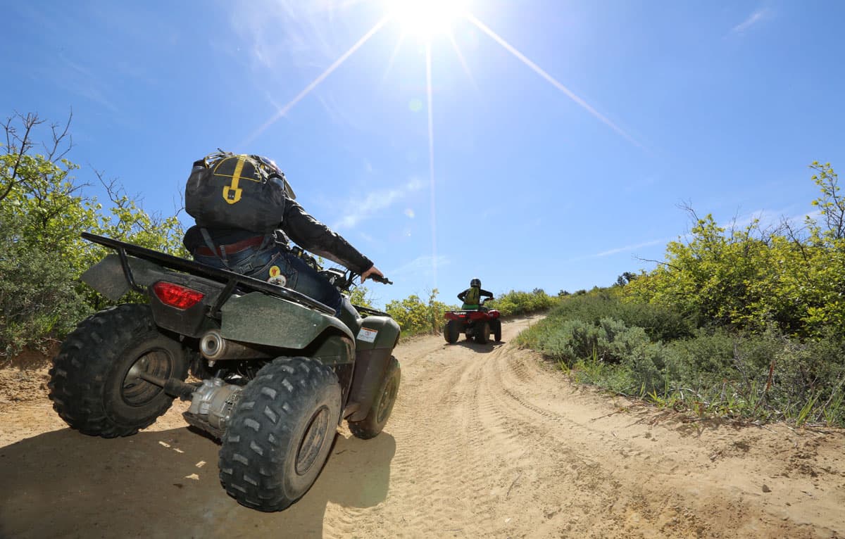 Two riders navigate a sandy trail on all-terrain vehicles under a bright sun.