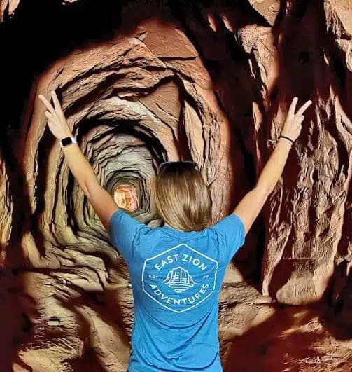 Person in a blue t-shirt stands in a tunnel, raising both hands in a peace sign.