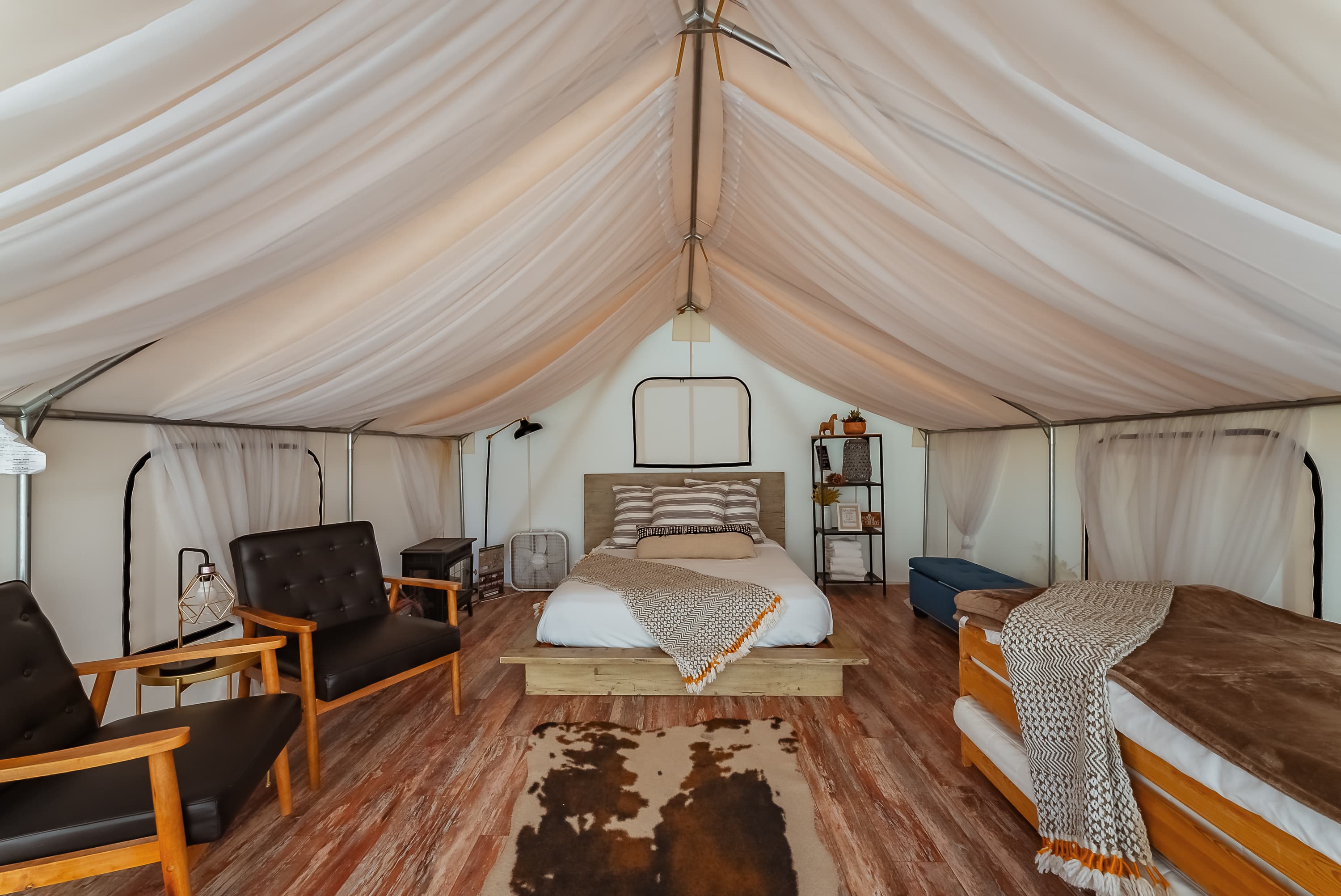 A cozy, spacious tent interior featuring a queen bed, armchairs, and a rustic decor.
