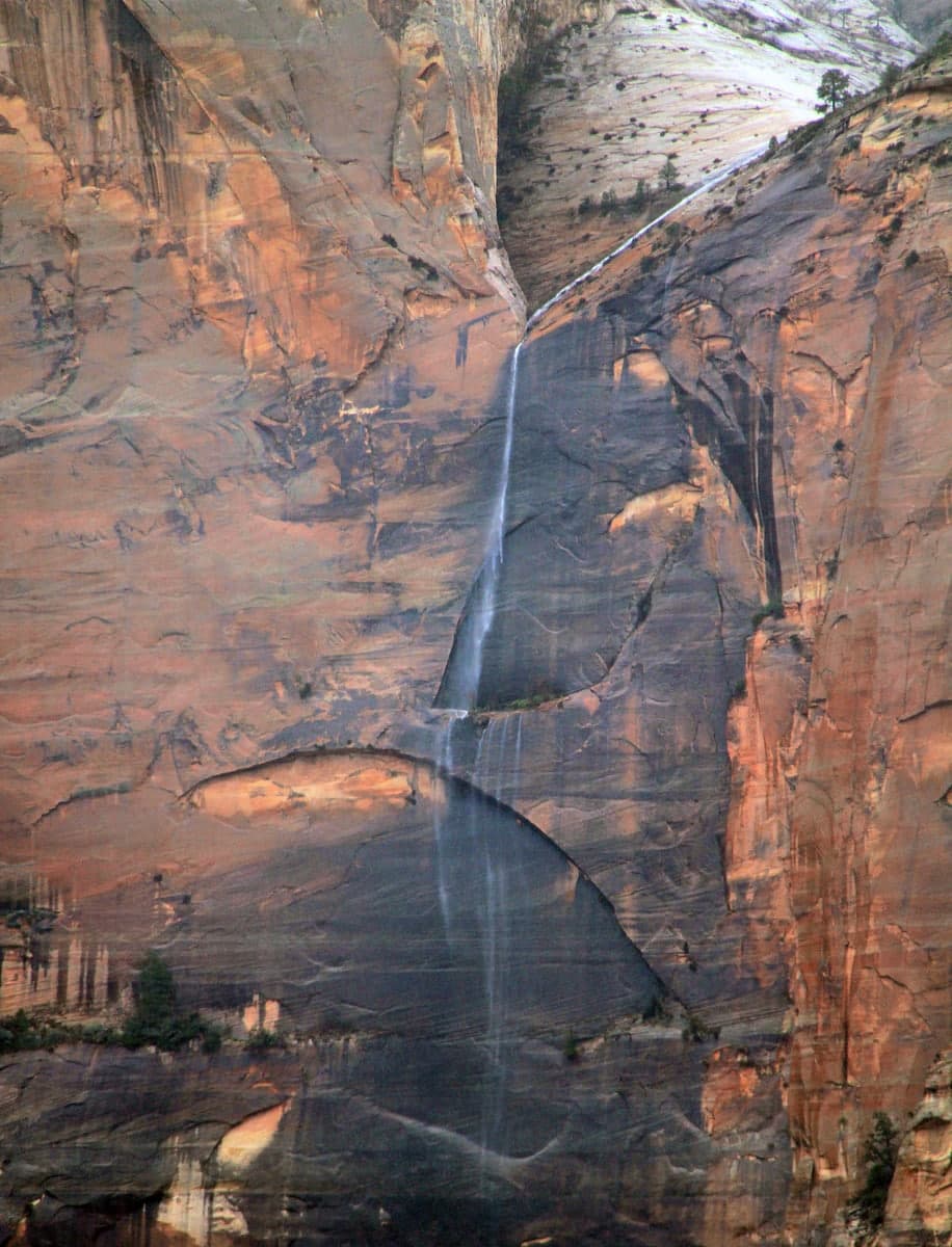 A waterfall cascades down a rocky cliff face in a desert landscape.
