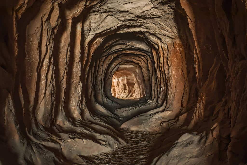 A dark, winding cave tunnel with textured rock walls and a lighted exit in the distance.