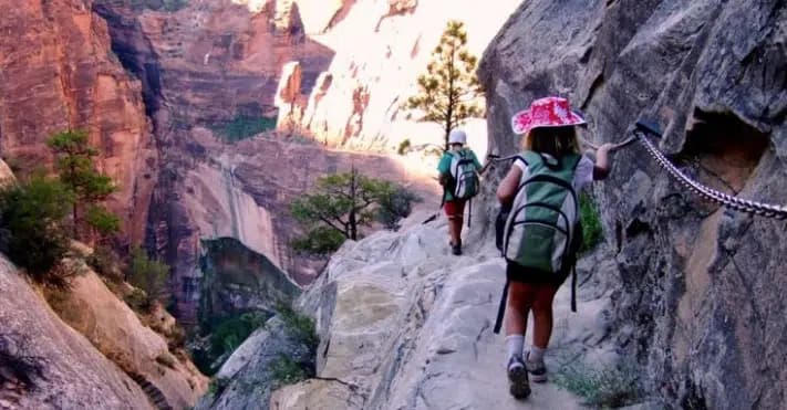 Two children hike along a rocky trail in a canyon, surrounded by steep cliffs.