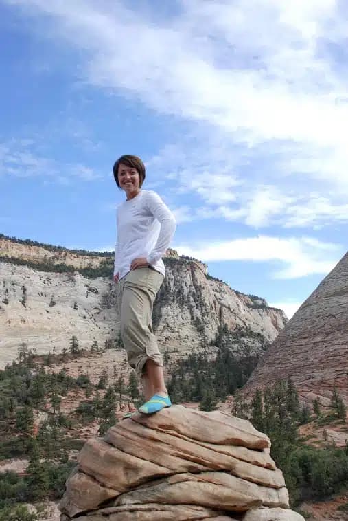 A woman standing on a rock with mountains and a blue sky in the background.