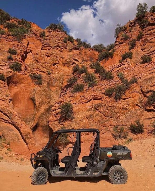 A black off-road vehicle parked in front of red rock formations and blue skies with clouds.
