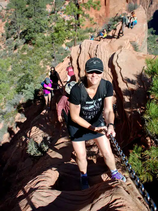 A group of hikers navigates a rocky trail, with one woman using a chain for support.
