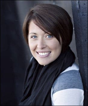 A smiling woman with short brown hair and blue eyes wearing a black scarf and a striped shirt.