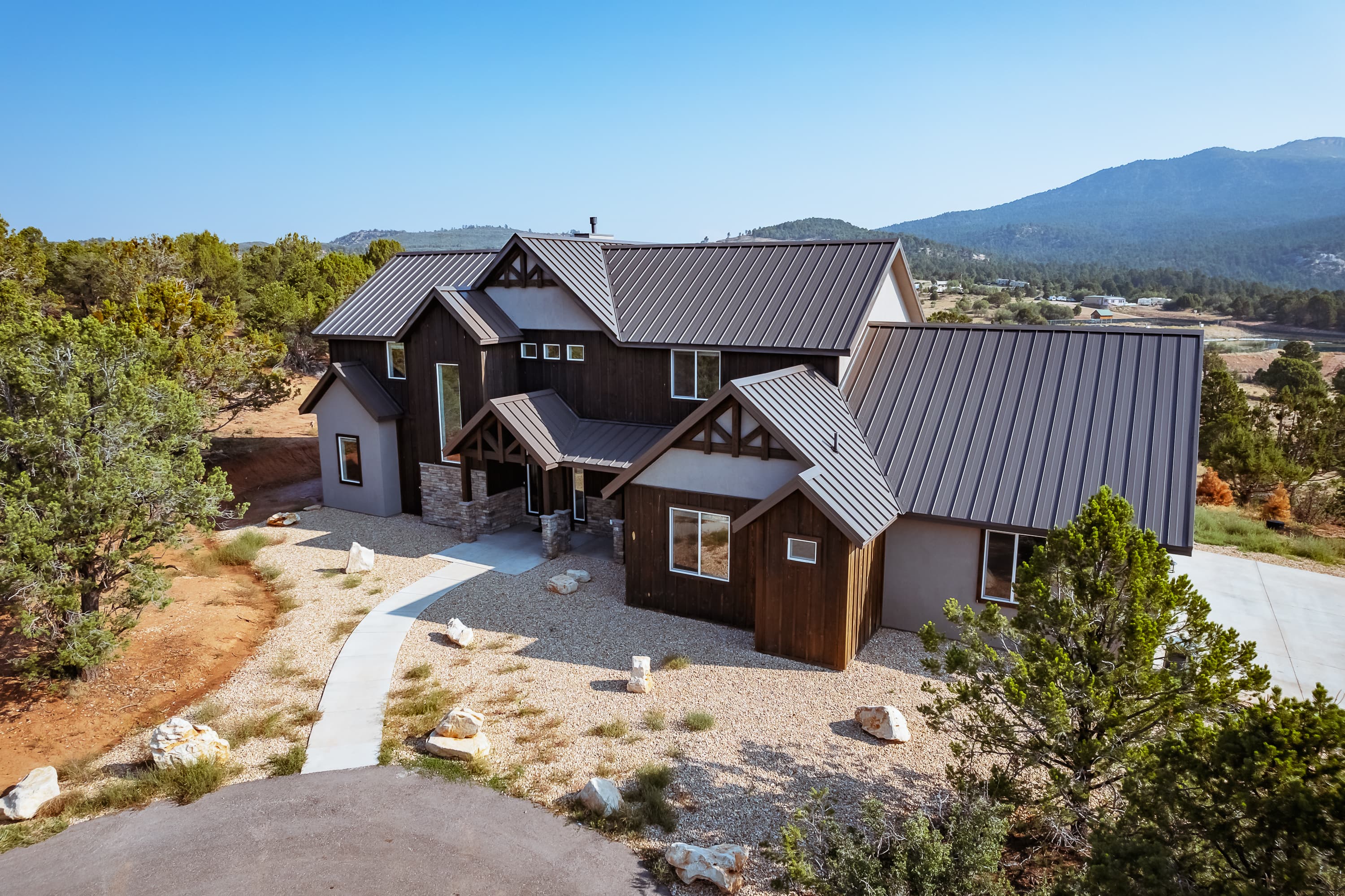 A modern house with a metal roof, surrounded by trees and mountains.