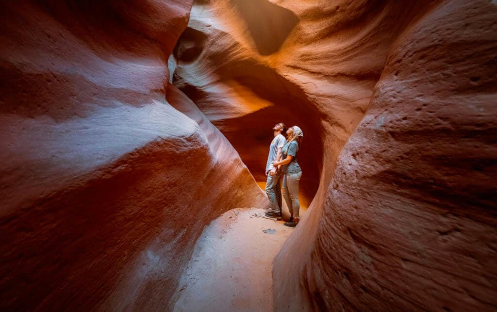 Two people admire the towering, red rock formations of a narrow canyon.