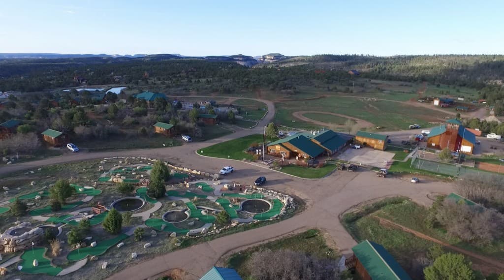 Aerial view of a resort area featuring a mini-golf course, several buildings, and surrounding green landscapes.