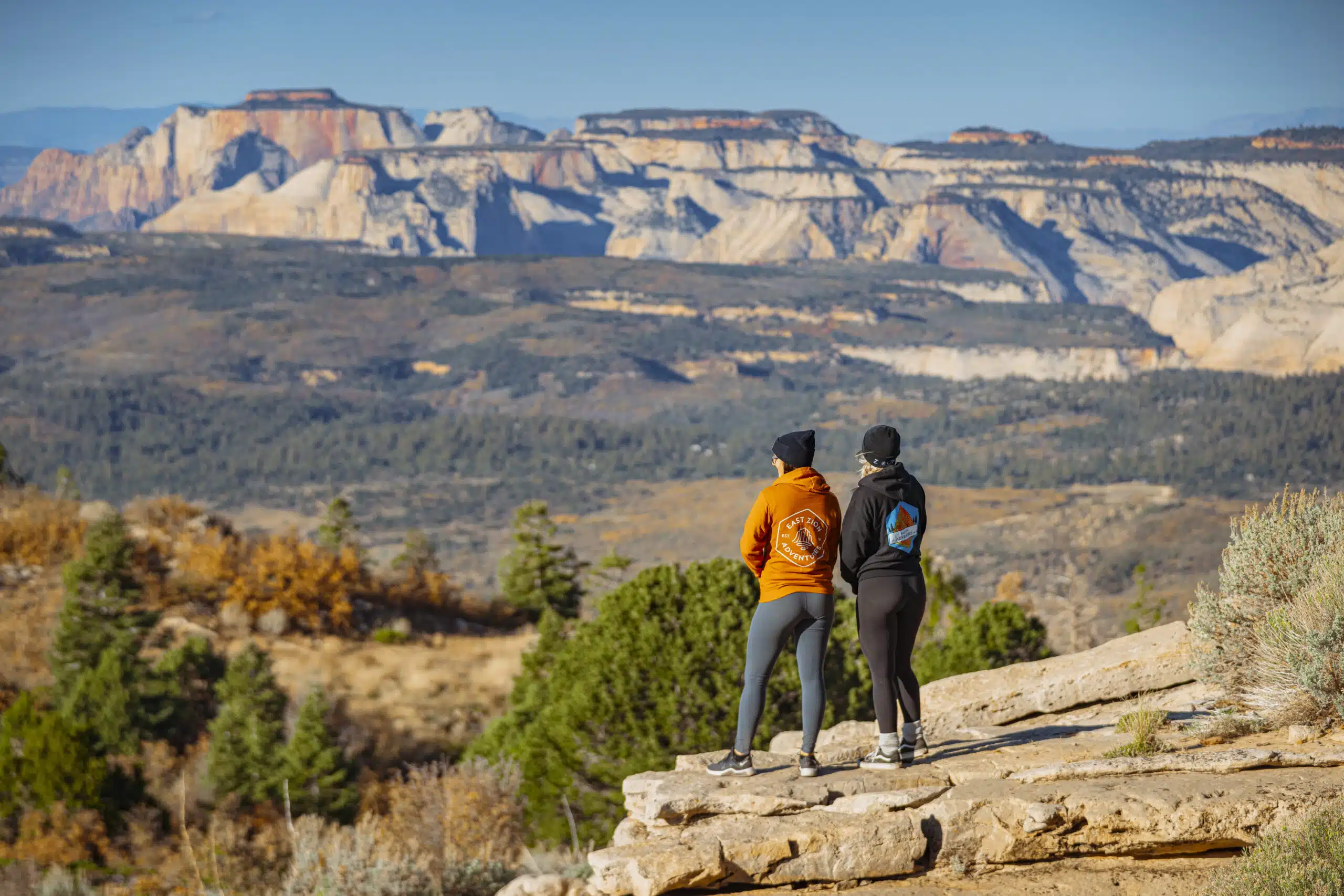 Two hikers admire a vast mountainous landscape from a rocky viewpoint.