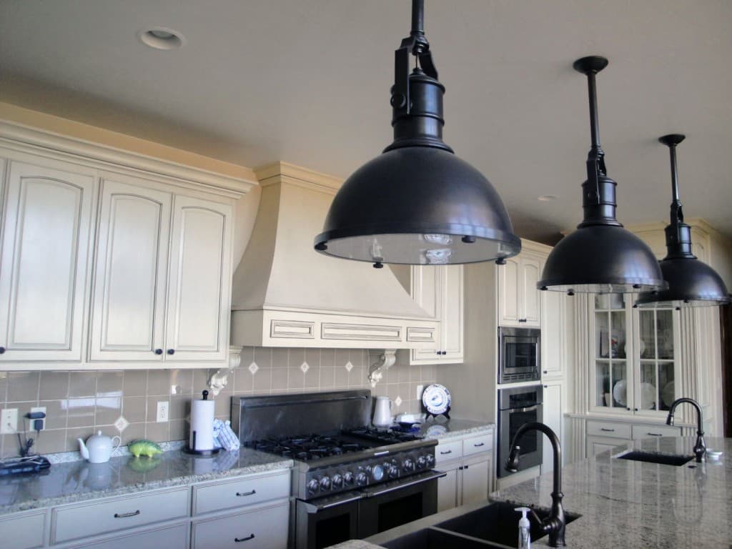 A modern kitchen featuring granite countertops, white cabinetry, and black pendant lights.