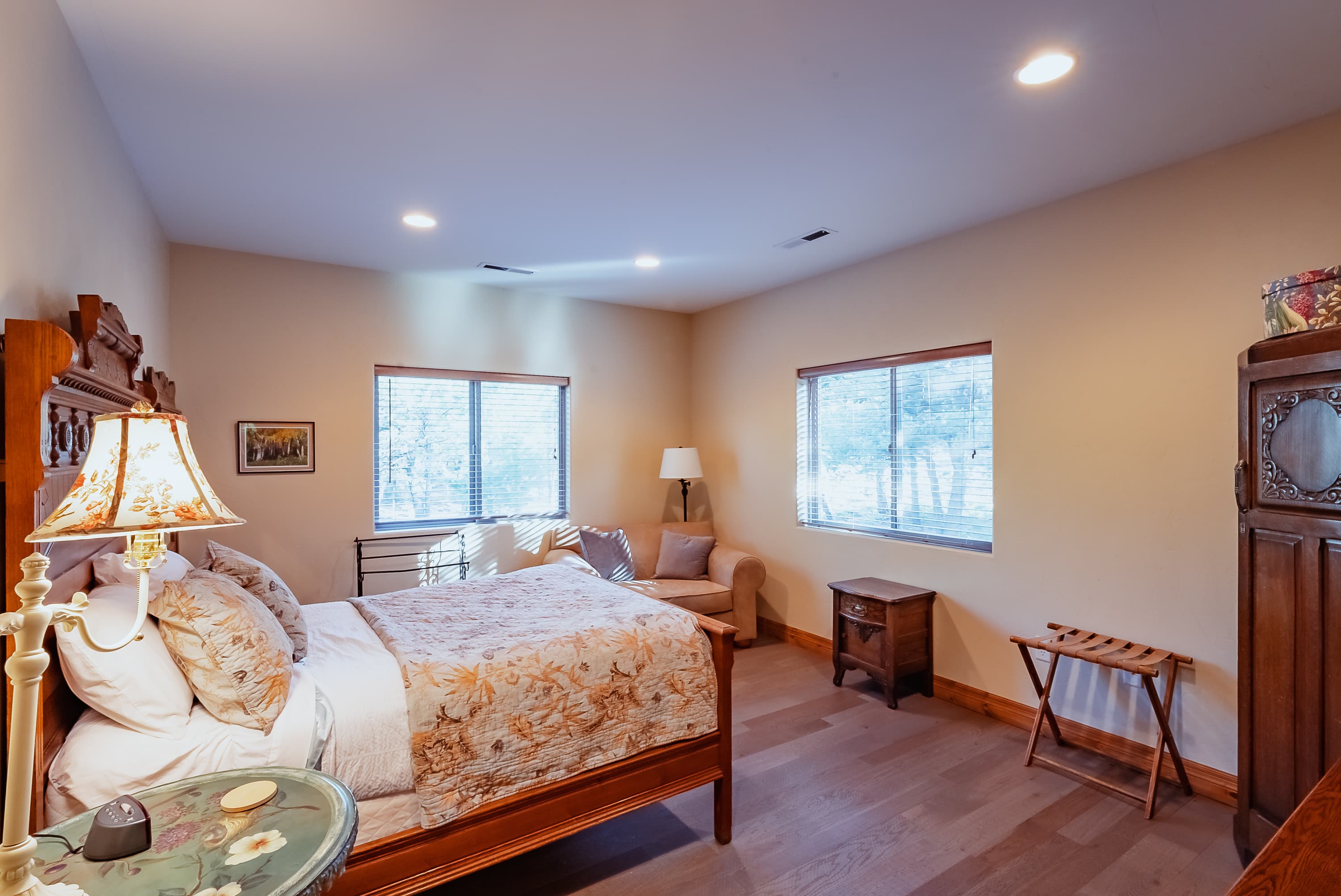 Cozy bedroom featuring a bed with floral bedding, a seating area, and large windows.