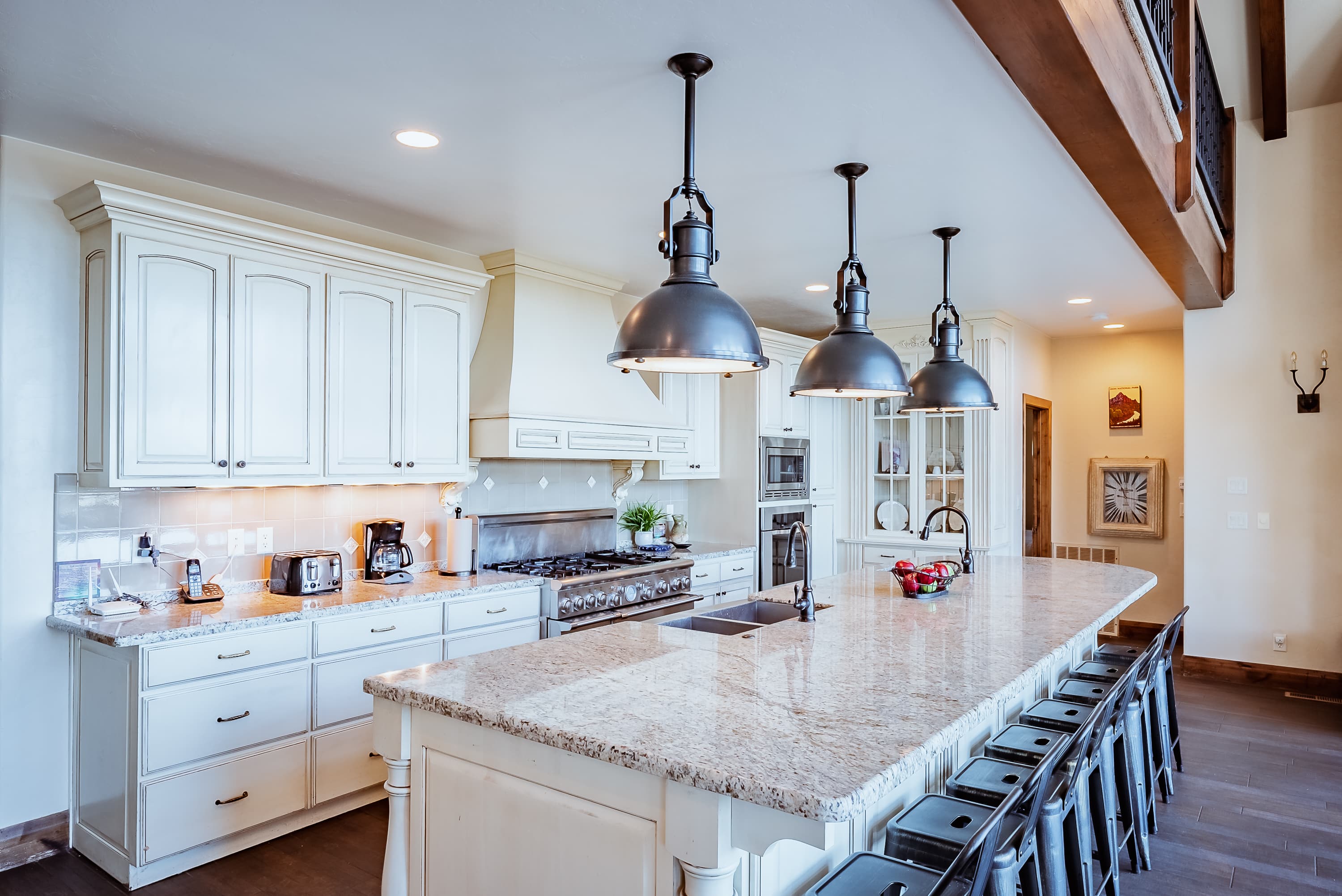 A modern kitchen featuring white cabinets, a large granite island, and industrial-style pendant lights.