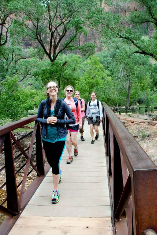 Five hikers cross a wooden bridge surrounded by lush greenery.