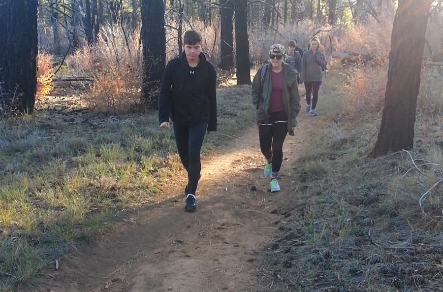 A group of four people walks along a dirt trail in a forested area.