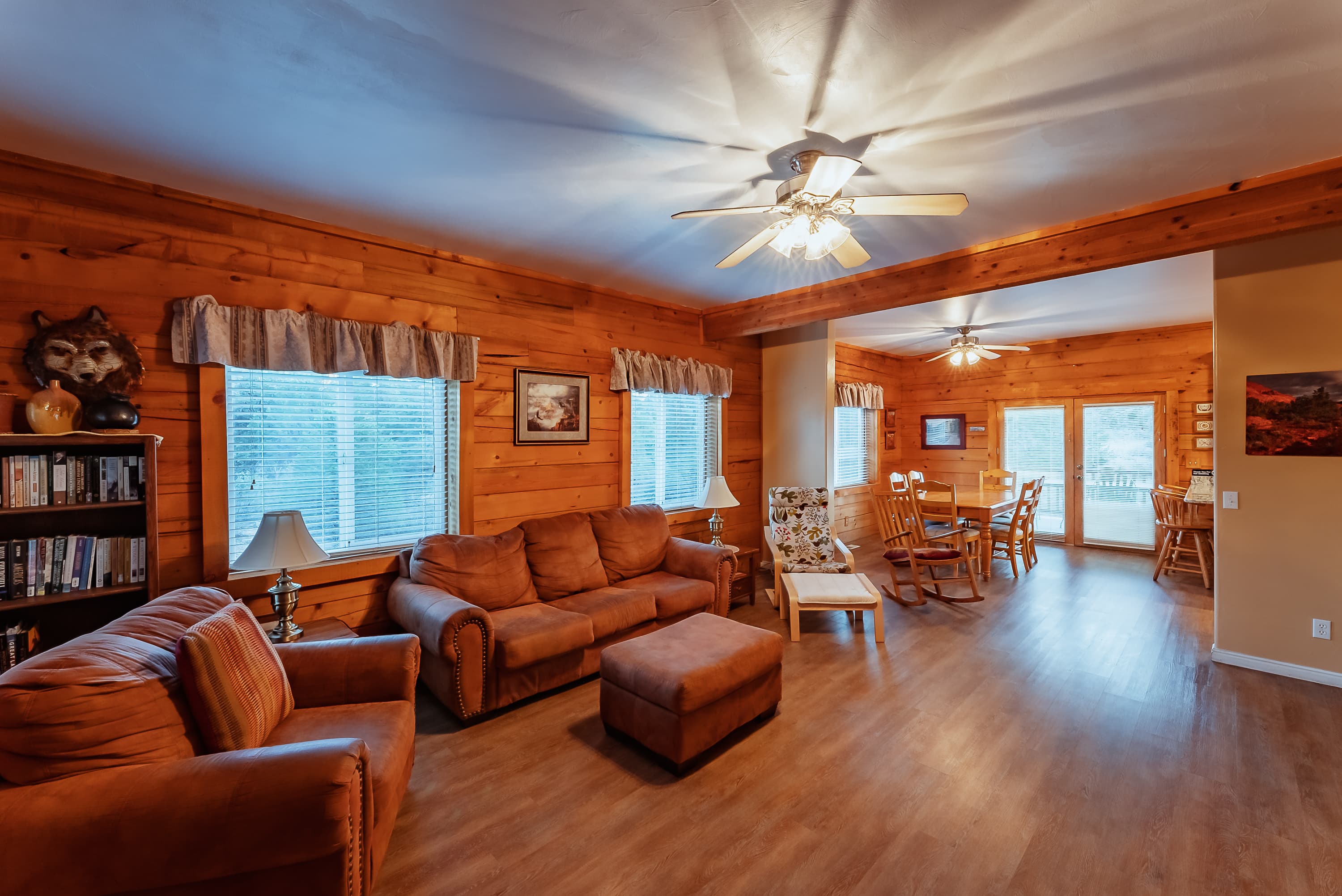 Cozy living room with wooden walls, a brown sofa, and a dining area visible through an open space.
