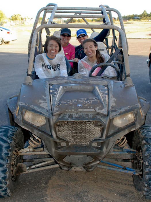 Four smiling women sitting in a muddy off-road vehicle.