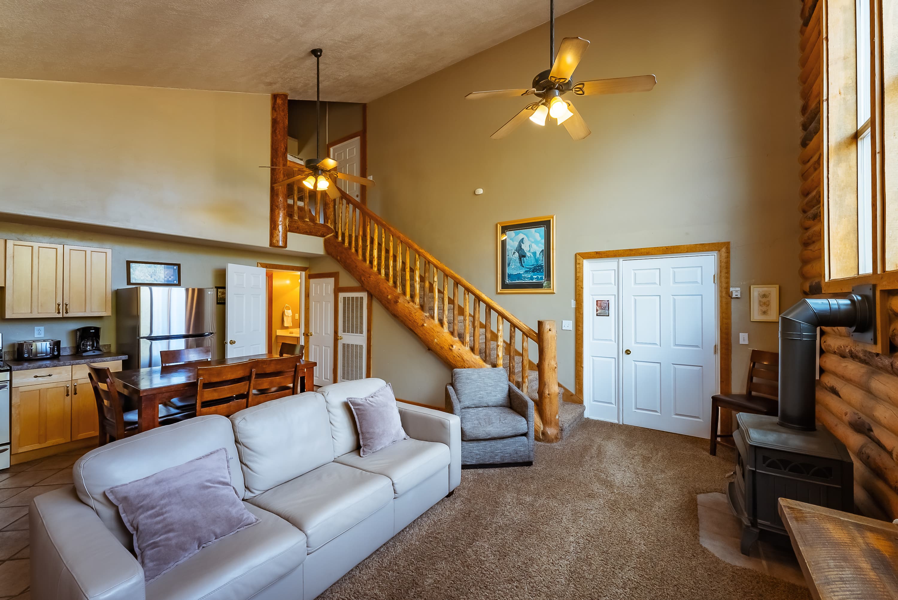 A spacious living room with a white sofa, wooden staircase, and kitchen area.