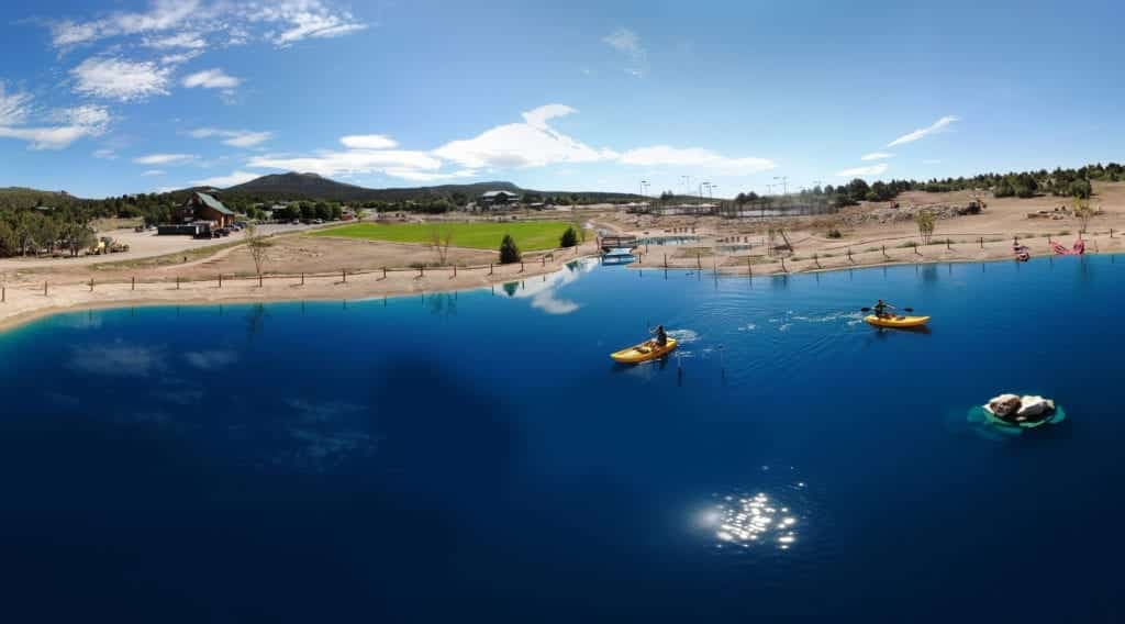 A panoramic view of a serene blue lake with kayakers and a scenic landscape in the background.
