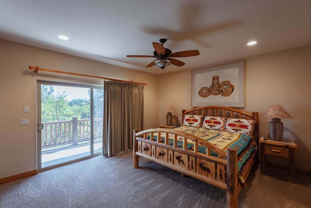 A cozy bedroom featuring a wooden bed, colorful quilt, and large sliding door leading to a balcony.