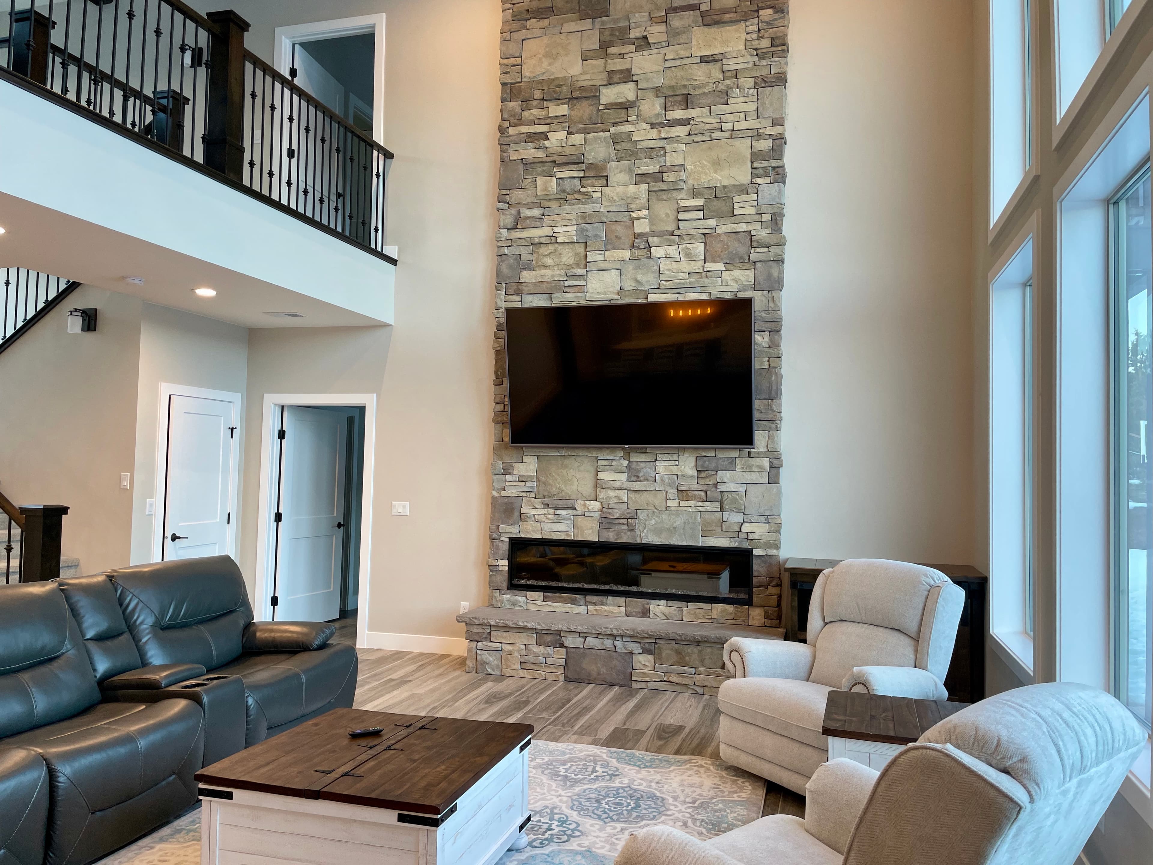 A modern living room featuring a stone fireplace, large windows, and comfortable seating.