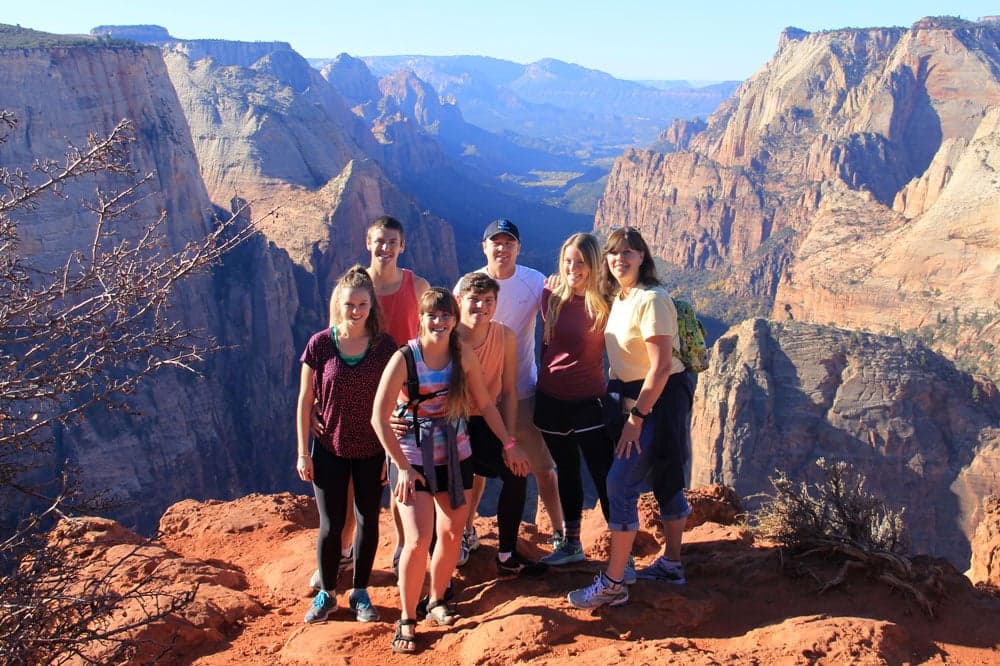 A group of seven people poses together at a scenic viewpoint in a mountainous landscape.