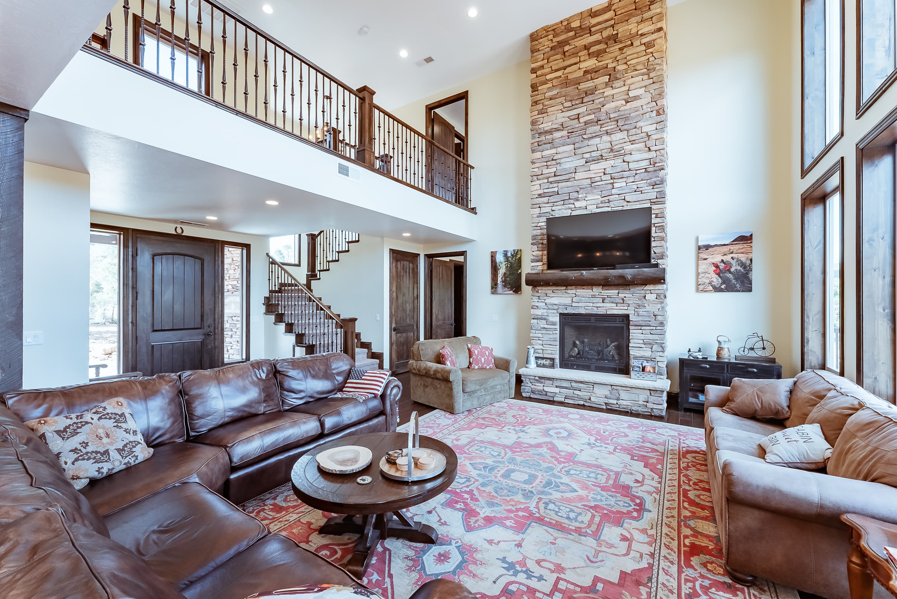 A spacious living room with a stone fireplace, large windows, and a cozy seating arrangement.