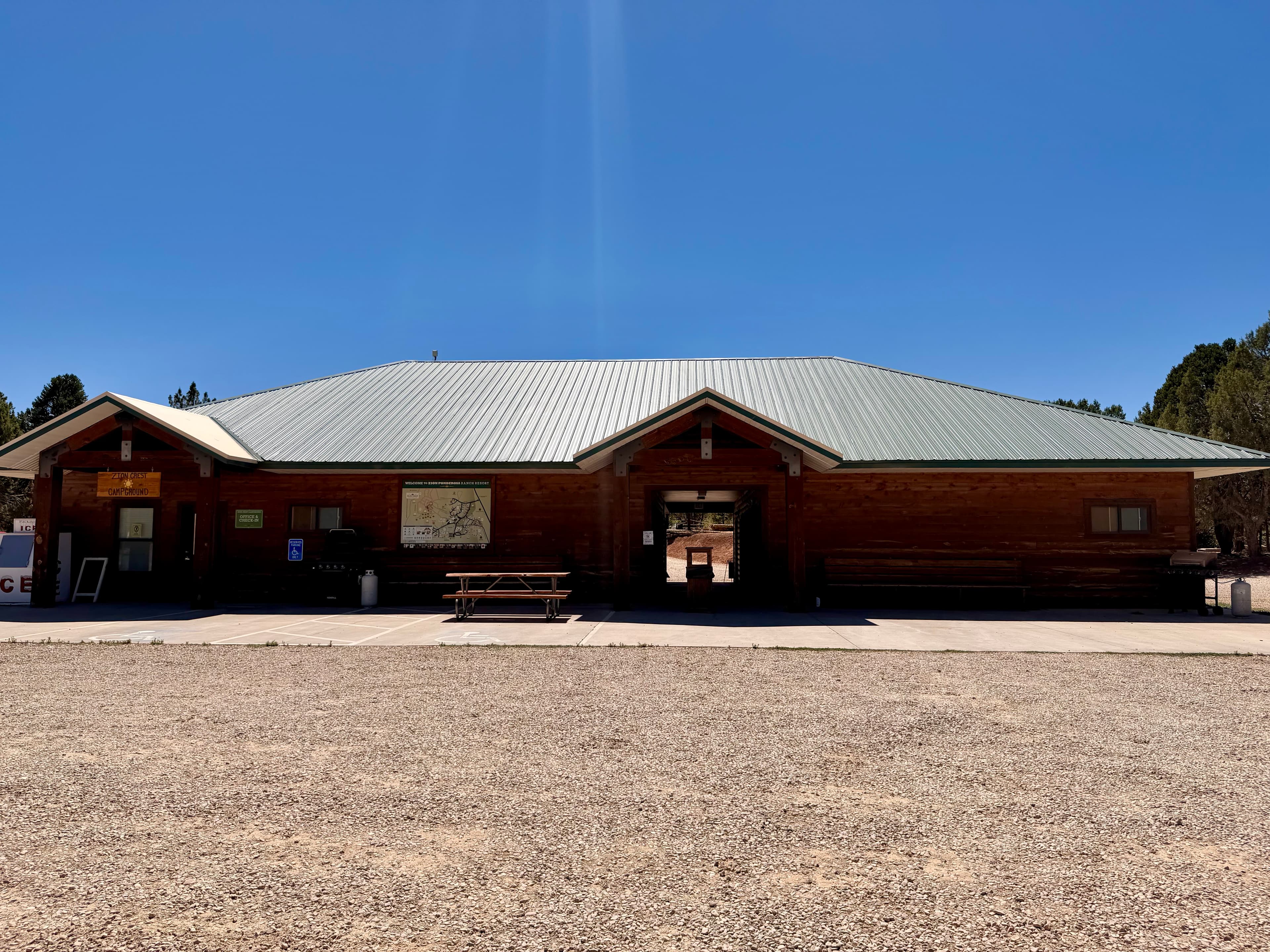 A wooden visitor center with a metal roof, surrounded by a gravel area under a clear blue sky.