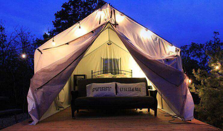 A cozy, illuminated tent with a bed and cushions, set against a twilight backdrop.