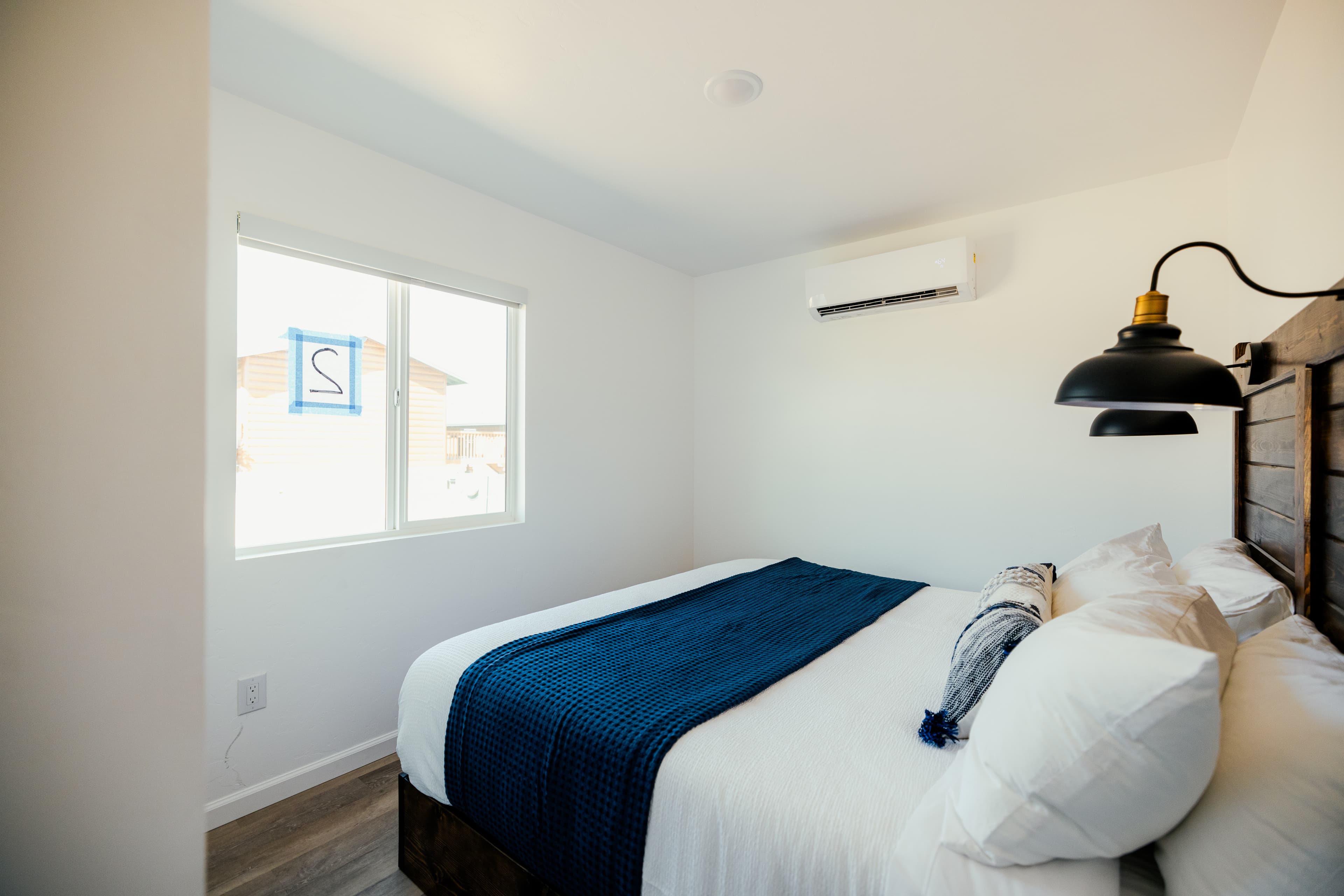 A bright and minimalist bedroom featuring a queen bed with a blue throw blanket and a window letting in natural light.