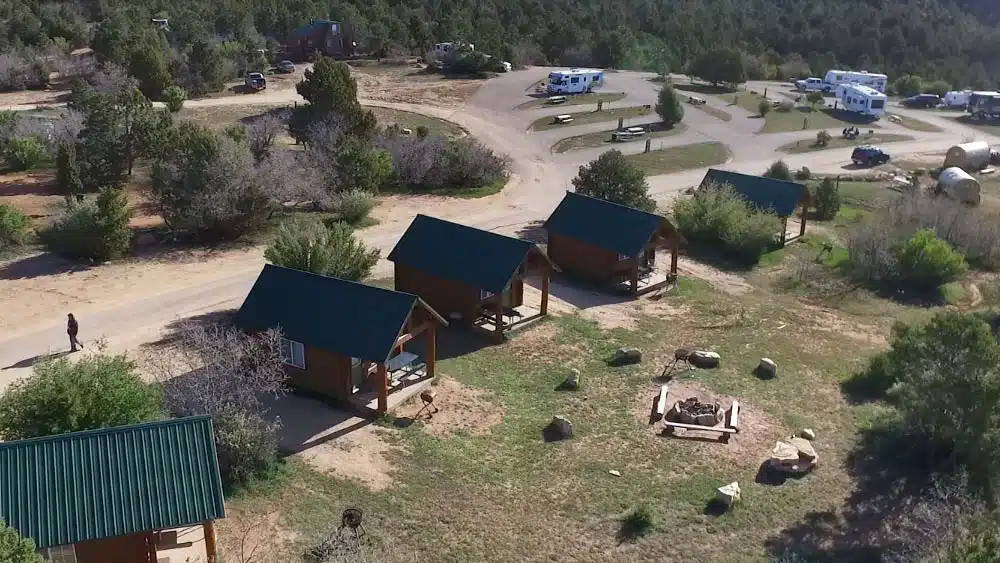 Aerial view of a campground with several cabins, a fire pit, and RVs in the background.
