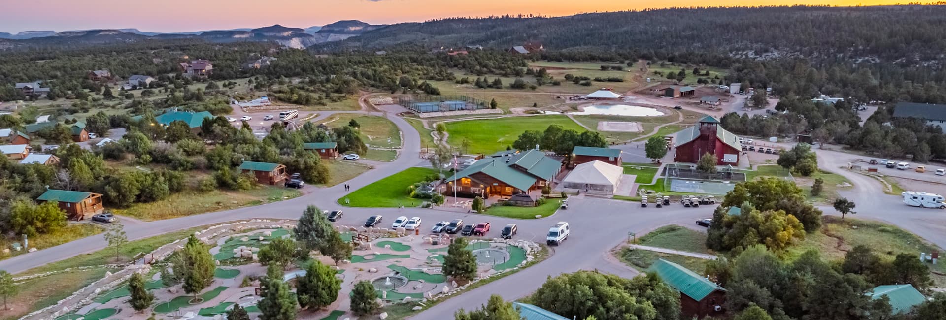 Aerial view of a mountainous landscape featuring a rustic lodge, parking area, and recreational facilities.