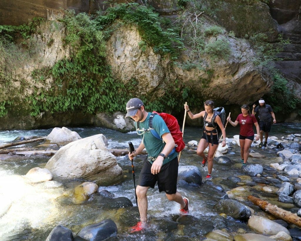 Four hikers navigating a rocky stream in a lush canyon.