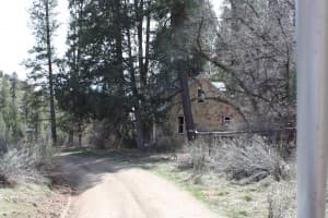 A dirt path leads to an old, stone house surrounded by tall trees.