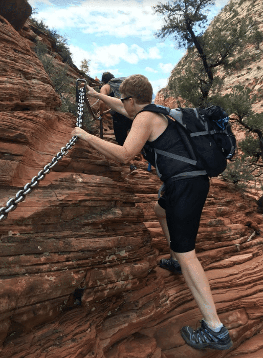 A hiker climbs a rocky terrain using a chain for support.