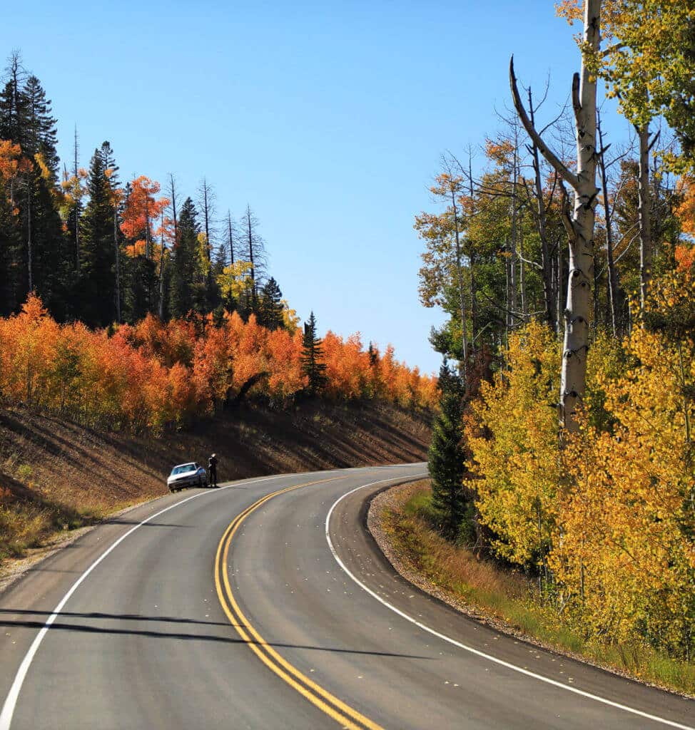 A winding road surrounded by vibrant fall foliage and a parked car.